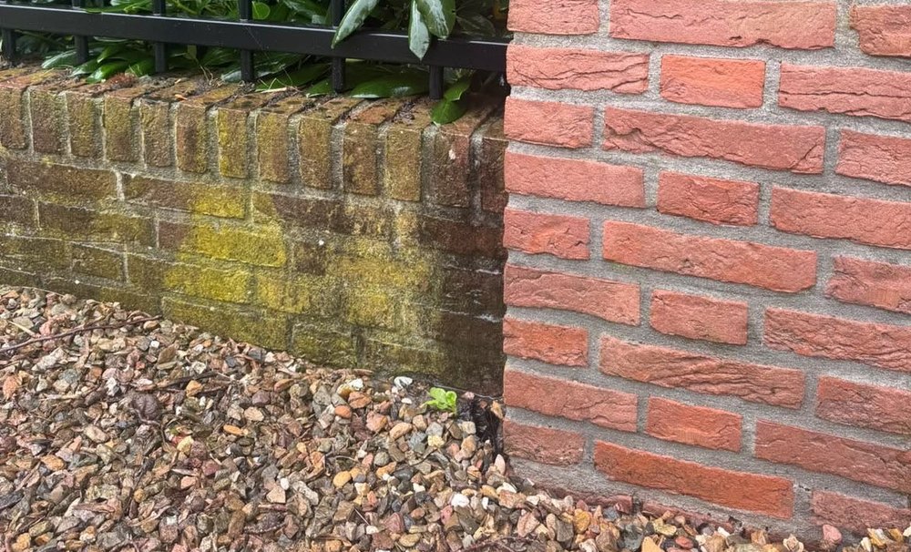 Tuinmuur met groene aanslag naast een gereinigde bakstenen pilaar